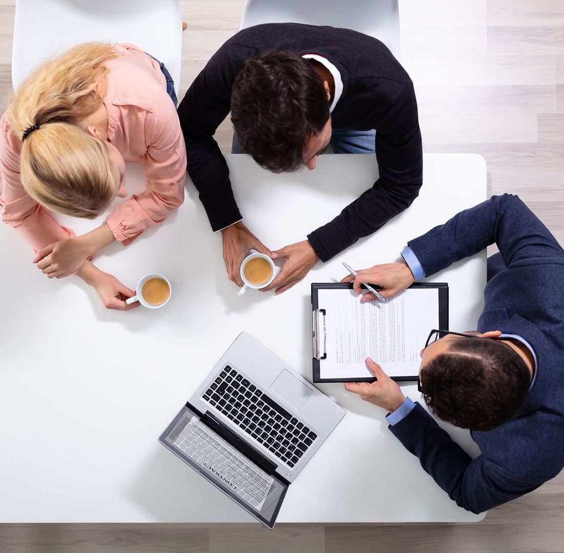Aufsicht auf 3 Leute die an einem Tisch sitzen und Vertragsinformationen besprechen